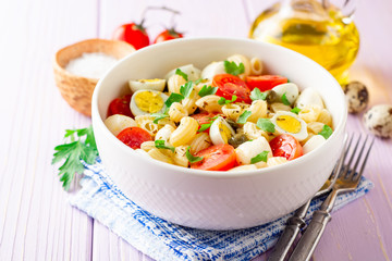 Pasta salad with quail eggs, mozzarella, cherry tomatoes and capers in bowl on purple wooden background