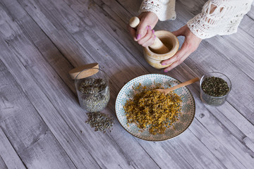 top view of woman hands with ingredients on table, wooden mortar, yellow turmeric, lavender and green natural leaves. Close up, daytime