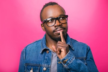 Emotions of a pensive African man wearing glasses on a pink background