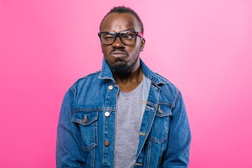 Fototapeta premium Scowling African man in glasses standing over pink background