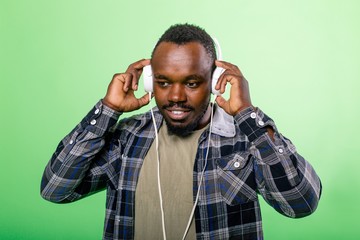 African man listening to music in headphones on a green background