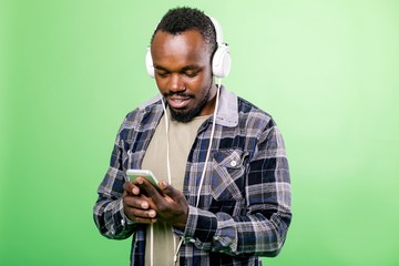 Young man listening to music in headphones through the phone standing on a green background