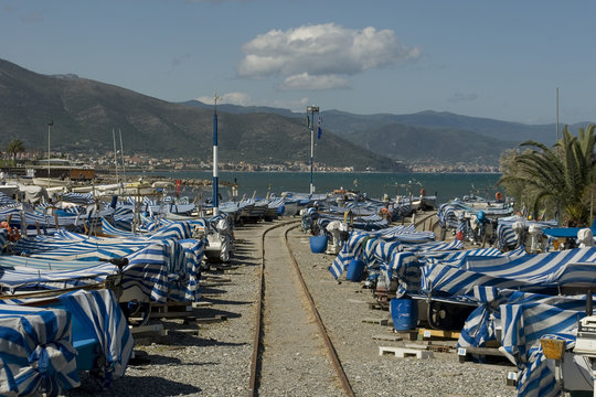 old fishing port, small wooden boats, covered with white and blue striped cloth, in the middle an iron track used to move boats to seashore, then put in water, summer, Albenga, Riviera, Liguria, Italy