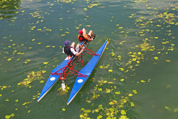 Man and woman ride with floating pedal bicycle boats across the lake