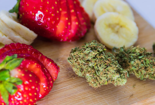 Trimmed marijuana bud up close with fresh strawberries and bananas