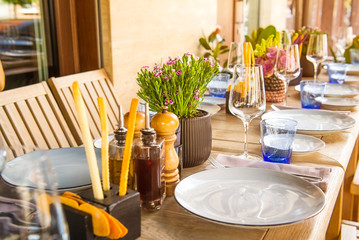 Light Table set for wedding or another catered event dinner. Wooden table served with plates, forks, spoons, glasses, napkins in the restaurant. Selective focus, space for text.
