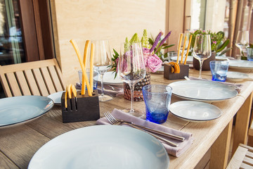 Light Table set for wedding or another catered event dinner. Wooden table served with plates, forks, spoons, glasses, napkins in the restaurant. Selective focus, space for text.