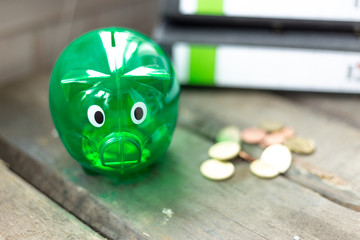 Grünes Sparschwein mit Münzen und Ordner auf einem Tisch