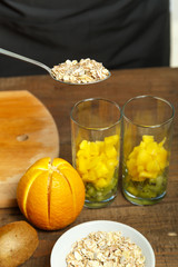a woman holds a spoon with flakes of muesli in her hand. prepares to pour muesli into glasses with fruit smoothies. vertical photo