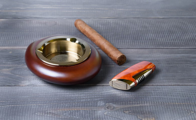 Stylish exquisite ashtray, cigarette lighter, Cuban cigar on a gray wooden background