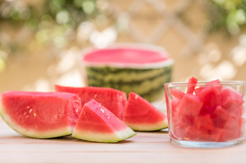 watermelon slices on wooden table and glass cup with pieces of watermelon, mediterranean garden background
