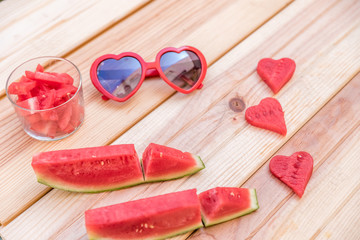 sliced ​​watermelon, glass cup with watermelon slices and red sunglasses with heart shape on wooden table