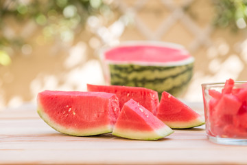 watermelon slices on wooden table and glass cup with pieces of watermelon, mediterranean garden background