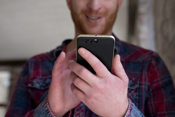 Man holding phone in his hands scrolling through news. Close up of young male with beard holding smart phone with dual camera.