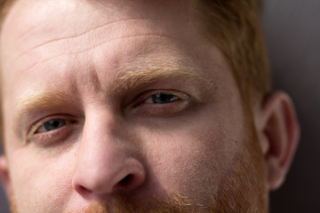 Man with beautiful blue eyes looking straight into camera. Close up of ginger man with beard looking in frame with calm face expression.