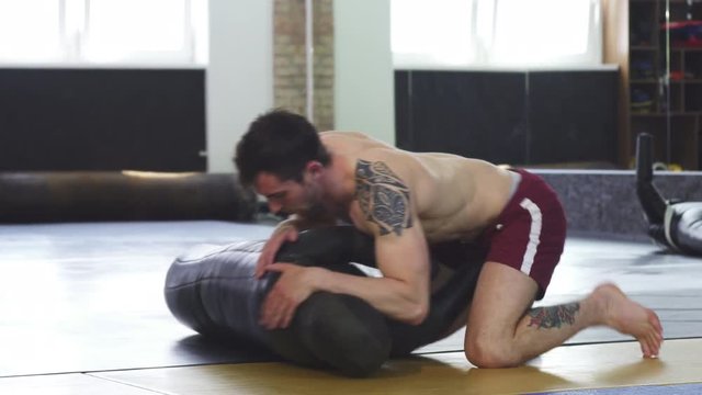 Shot of a handsome muscular tattooed wrestler working out at the gym, practicing side control movements. Mixed martial arts training. Sports and motivation. Active lifestyle and strength.