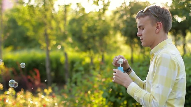 Young man blowing soap bubbles in the garden