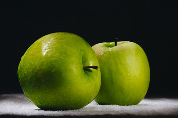 two fresh green apples on a dark background.