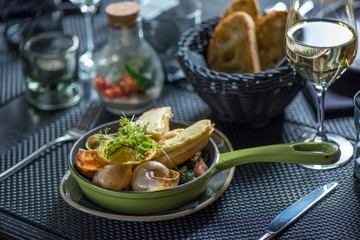 Frying pan with escargot snails with garlic butter, rustic wooden surface, selective focus