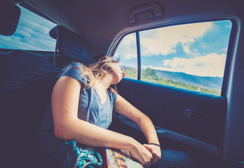 Woman teenager with long hair sleeping in the backseat of a car on a trip after reading the guide book