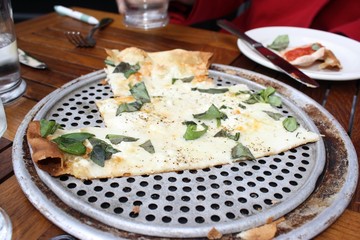 Eating cheese pizza with white sauce and basil at a restaurant