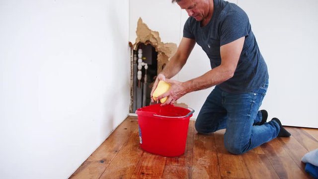 Mature Man At Home Mopping Up Water From Leaking Pipe