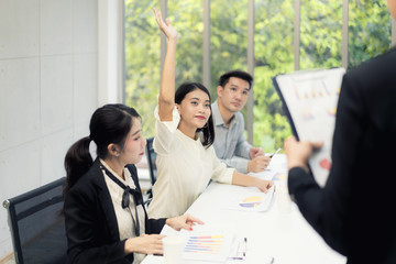 Asian woman is raising her hands has question while businessman presentation about business sale report at the meeting room