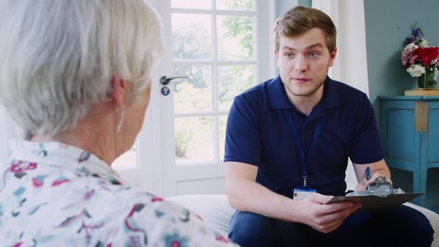 Senior woman talking with male care worker on home visit
