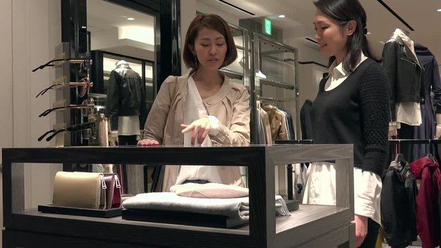 Asian people shopping for fashion goods and accessories. Japanese woman in luxury shop inside mall. Lady buying leather wallet in store and talking to sales assistant for help and assistance