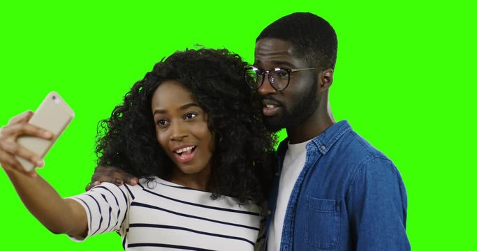 Close up of the smiled young African American couple taking nice selfie on the smartphone on the green screen background. Chroma key.