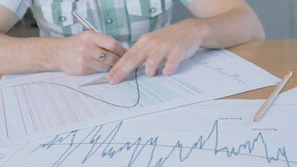 Young male employee working with documents sitting at table in company, man doing job with financial project, writing on workplace in modern interior. Concept: work day, documentation, professional.