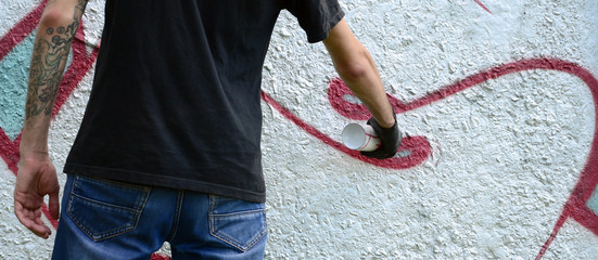 A young hooligan paints graffiti on a concrete wall. Illegal vandalism concept. Street art