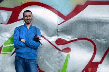 The graffiti artist with spray can poses against the background of a colorful painted wall. Street...