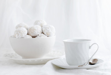 Photograph of white Snowball cookies with a white cup and saucer on white