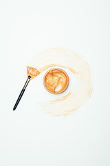 top view of golden mask in container surrounded by smudge with brush isolated on white surface