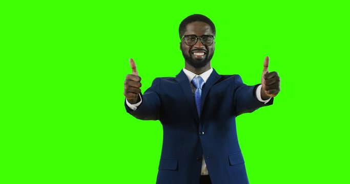 Attractive cherful African American man in glasses, suit and tie giving his thumbs up while standing on the green screen background. Chroma key.