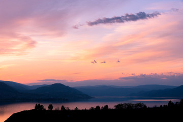 Obraz premium Evening view of sunset sky over lake with sihouettes of mountains and trees