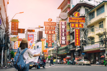 Junge asiatische Reisende mit blauem Rucksack und Hipster-Hut, die Karte auf der Straße mit Tuk-Tuk-Thailand-Hintergrund in China Town Bangkok suchen. Reisen in Bangkok Thailand