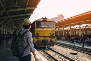 Young asian man traveler with backpack and hat standing and holding map waiting train for travel at train station in Bangkok city Thailand. Traveling in Bangkok Thailand