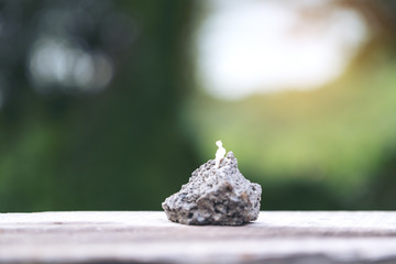 Closeup image of miniature figure model of a lonely woman sitting on the rock with blur background