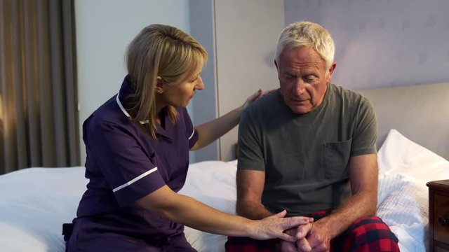Nurse Talking With Unhappy Senior Man In Bedroom On Home Visit