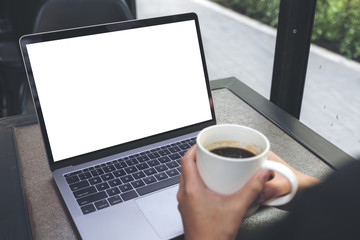 Fototapeta premium Mockup image of a woman using laptop with blank white desktop screen while drinking hot coffee in cafe