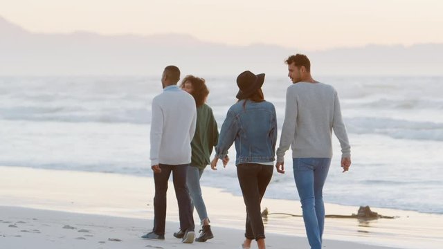 Rear View Of Friends Walking Along Winter Beach Together