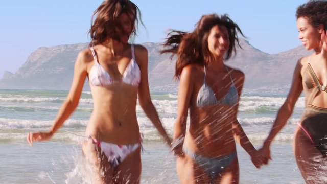 Female Friends Have Fun Running Through Waves On Beach Vacation
