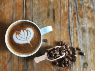 Love coffee in White coffee, latte art coffee cup and roast beans coffee in wooden spoon on the vintage wooden table with natural sunlight.