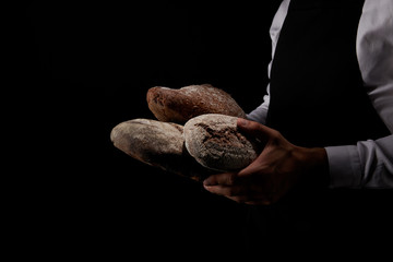 cropped image of male baker in apron holding various types of bread isolated on black background