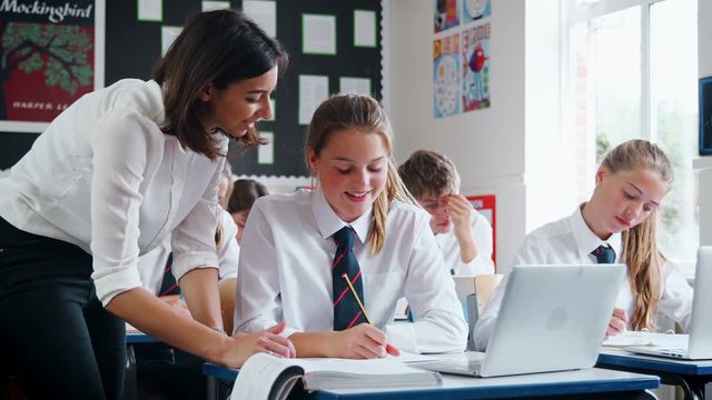 Teacher Helping Female Pupil Using Computer In Classroom