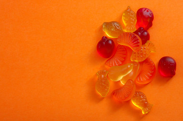 Unhealthy eating and gelatin-based chewable sweets concept with close up on a bunch of colorful fruit shaped gummy candy or jelly candies isolated on orange background