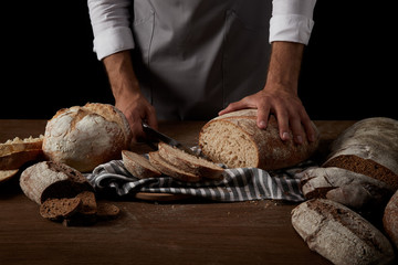 cropped image of baker in apron cutting bread on sackcloth on wooden table