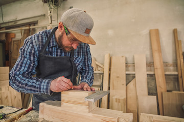Close-up of craftsman hands in gloves measuring wooden plank with ruler and pencil on workbench....